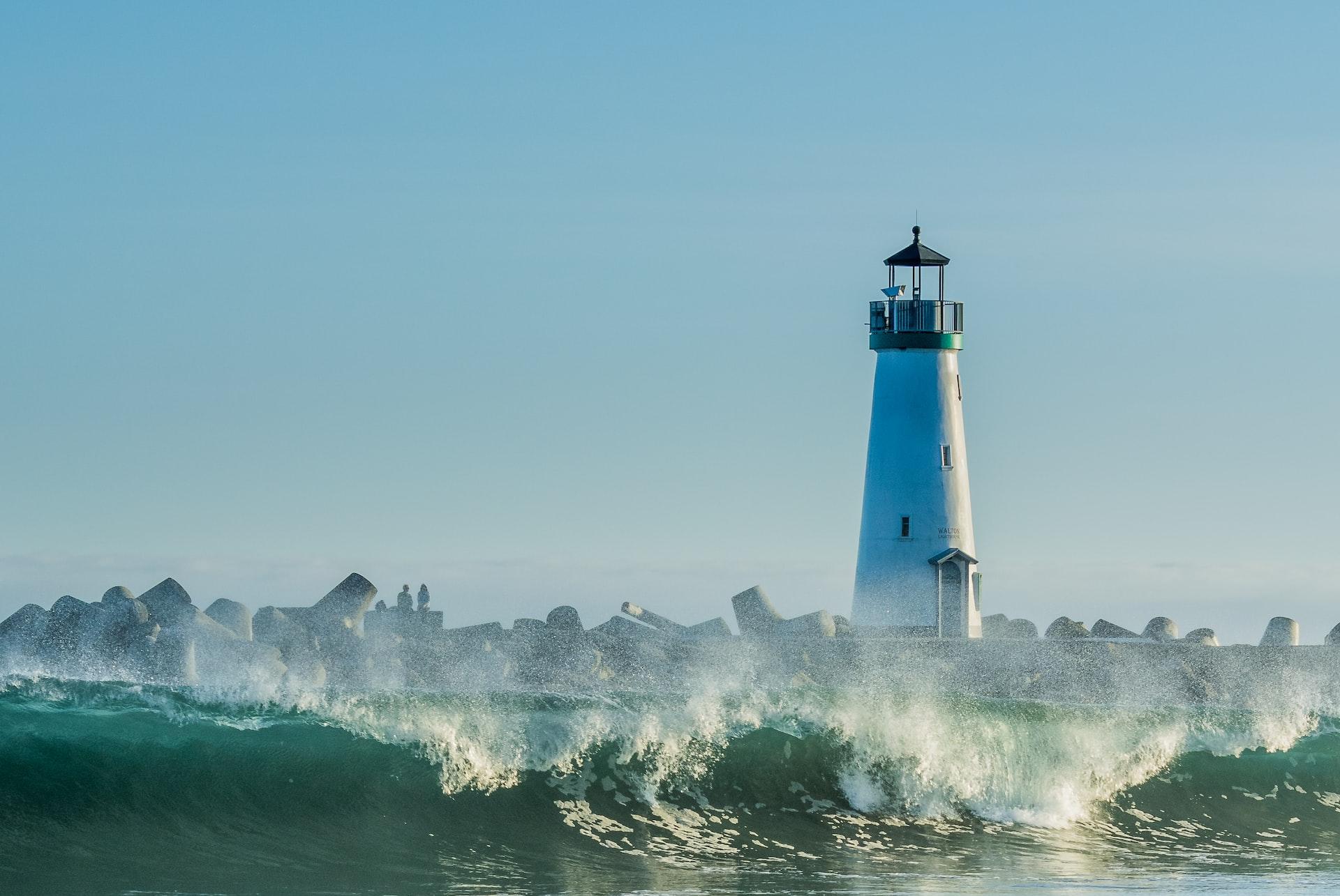 concrete lighthouse near rocks and ocean wave at daytime